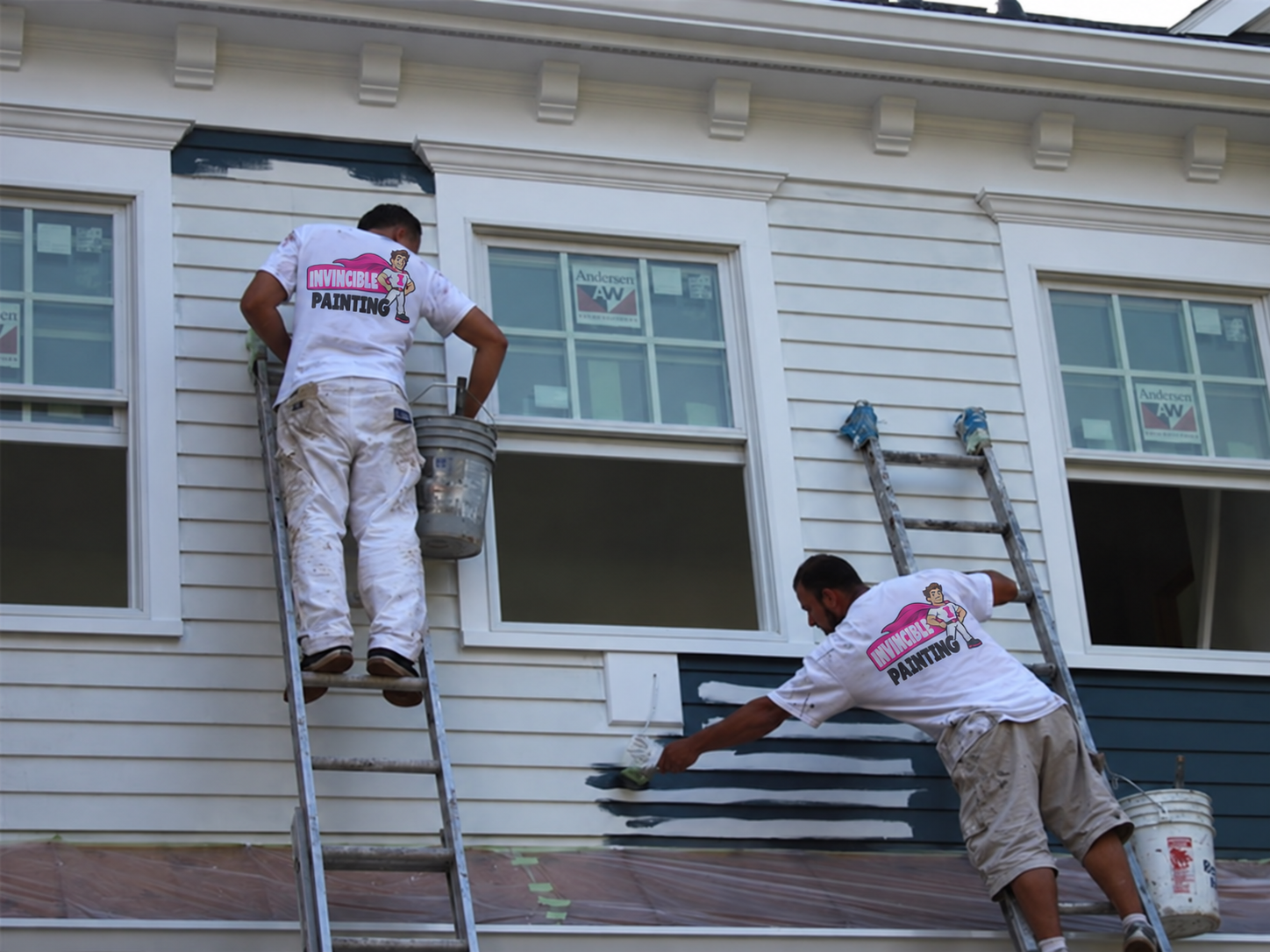 Two painters wearing Invincible Painting shirts working on house siding